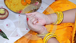 Beautiful Indian bride holding marigold flower in hands during a pooja for marriage wearing orange saree with yellow bangles