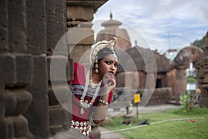 Beautiful indian girl dancer in the posture of Indian dance peeking around wall.Indian classical dance Odissi.