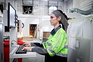Beautiful industrial female mechanic engineer in safety vest using computer to operate machinery at manufacturing plant factory,