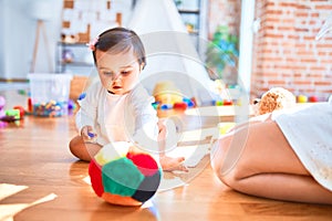 Beautiful infant happy at kindergarten around colorful toys