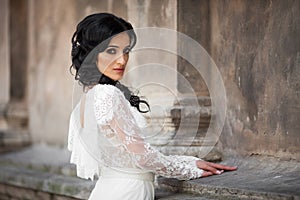 Beautiful innocent brunette bride in white dress posing near church wall