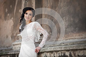 Beautiful innocent brunette bride in white dress posing near church wall