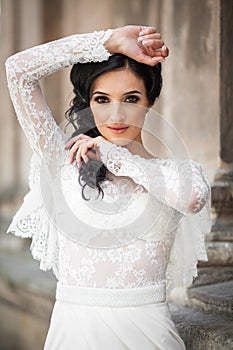 Beautiful innocent brunette bride in white dress posing near church wall