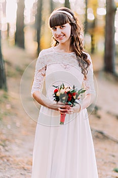 Beautiful innocent young brunette bride in gorgeous white dress with bouquet of flowers at forest