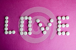 Beautiful inscription love made from white round smooth medical pills, vitamins, antibiotics and copy space on a bright purple