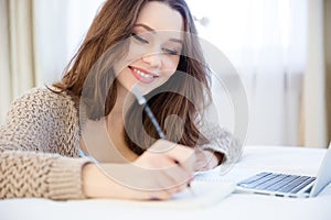 Beautiful inspired smiling young woman writing in notepad