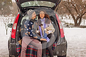 Beautiful international couple relaxing in nature in winter. Romantic meeting of a couple in love in the snow. Young couple sit in