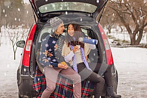 Beautiful international couple relaxing in nature in winter. Romantic meeting of a couple in love in the snow. Young couple sit in