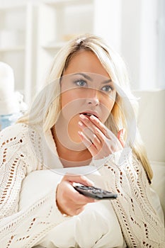 Beautiful intrigued woman watching TV using remote control