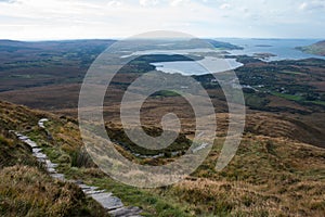 Beautiful irish landscape seen from the top of a hill. Green fields, stone path and the athlantic ocean in the background