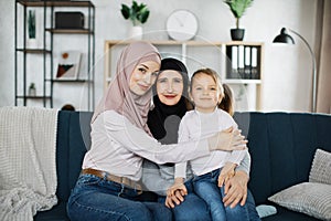 Beautiful islamic women generation: granny, mom and daughter are hugging, looking at camera