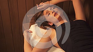 Beautiful isolated hot woman is lying on benc at steam room on white towel for skin wellbeing therapy.