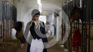 beautiful jockey woman is walking in stable, smiling broadly to camera