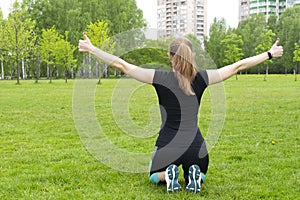 Beautiful joyful girl after fitness training kneels holds her hands in different directions and shows thumbs up. View from the