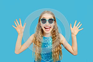 Beautiful joyful little Caucasian girl in a blue dress looks into the camera. She shows her hands and rejoices. Isolated