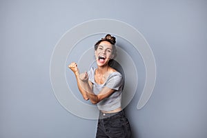 Beautiful joyful shouting woman hands up celebration win over gray background