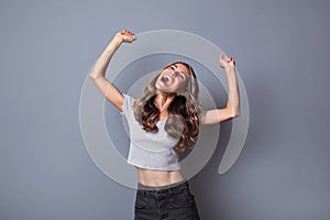 Beautiful joyful shouting woman hands up celebration win over gray background