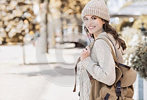 Beautiful joyful woman autumn portrait. Smiling student girl wearing warm clothes and hat in a city in winter