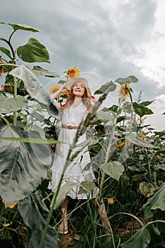 Beautiful joyful woman in blooming sunflower field. Smiling girl with sunflower on field, outdoors. Girl in light beige