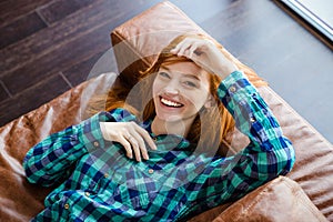 Beautiful joyful woman laying on brown sofa and laughing