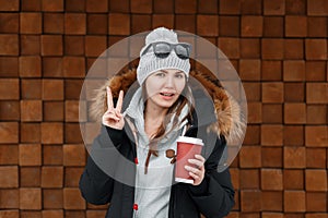 Beautiful joyful young hipster woman in vintage knitted hat in a stylish winter jacket with fur in a gray trendy sweatshirt