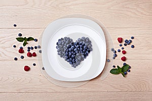 Beautiful juicy ripe natural organic raspberries blackberries blueberries and mint blue tablecloth dots white dish heart shape