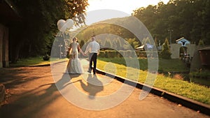 Beautiful just married couple with balloons walking at the golden autumn park and softly kissing on sunset