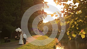 Beautiful just married couple with balloons walking at the golden autumn park on sunset