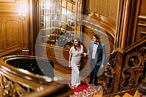 Beautiful just married walking up by amazing stairs with the background of royal wooden vintage interior