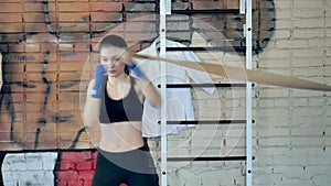 Beautiful kickboxing woman training punching with rubber band in fitness studio fierce strength fit body kickboxer