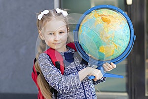 Beautiful kid back to school. Smart schoolchild with red schoolbag holding globe in hands. Education