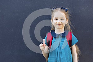 Kid back to school. Happy pupil girl standing at blackboard with chalk in hand. cute confident schoolgirl with backpack i