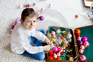 Beautiful kid boy and colorful vintage xmas toys and ball in old suitcase. Child decorating Christmas tree