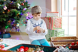 Beautiful kid boy and colorful vintage xmas toys and balls. Child decorating Christmas tree