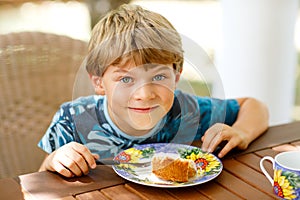 Beautiful kid boy eating apple pie in restaurant on vacations. Happy healthy child in an outdoor cafe in summer time