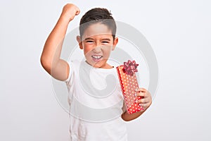 Beautiful kid boy holding birthday gift standing over isolated white background annoyed and frustrated shouting with anger, crazy