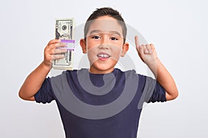 Beautiful kid boy holding dollars standing over isolated white background surprised with an idea or question pointing finger with