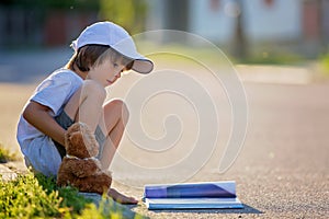 Beautiful kid boy, reading a book on the street, sitting down wi