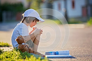 Beautiful kid boy, reading a book on the street, sitting down wi