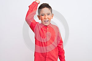 Beautiful kid boy wearing elegant red shirt standing over isolated white background angry and mad raising fist frustrated and