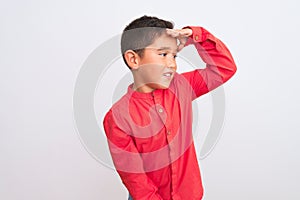 Beautiful kid boy wearing elegant red shirt standing over isolated white background very happy and smiling looking far away with