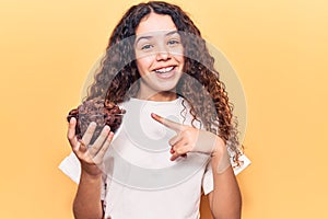 Beautiful kid girl with curly hair holding chocolate cereals smiling happy pointing with hand and finger