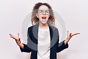 Beautiful kid girl with curly hair wearing business clothes and glasses crazy and mad shouting and yelling with aggressive