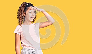 Beautiful kid girl with curly hair wearing casual clothes very happy and smiling looking far away with hand over head