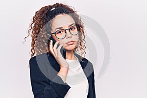 Beautiful kid girl with curly hair wearing glasses having conversation talking on the smartphone thinking attitude and sober