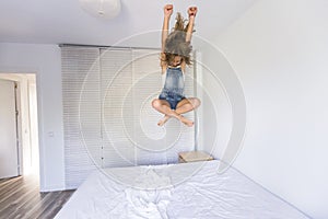 Beautiful kid girl playing and jumping on bed. Fun indoors. Family love and lifestyle