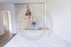 Beautiful kid girl playing and jumping on bed. Fun indoors. Family love and lifestyle