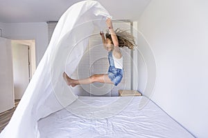 Beautiful kid girl playing and jumping on bed. Fun indoors. Family love and lifestyle