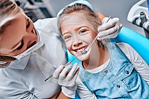 Beautiful kid girl smiling in dentist`s chair the office treats teeth. Doctor mask and child looks at camera