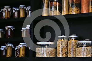 Beautiful kitchen glass jars for storing bulk products on a dark shelf with cereals, pasta, spices and beans